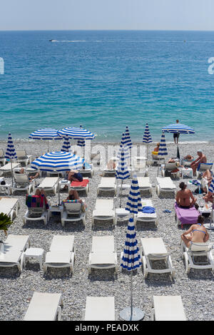 NICE, FRANCE - 26 MAI 2018- voir de parasols et chaises longues avec rayures bleu et blanc sur la plage de galets au-dessous de la Promenade des Anglais le long de t Banque D'Images