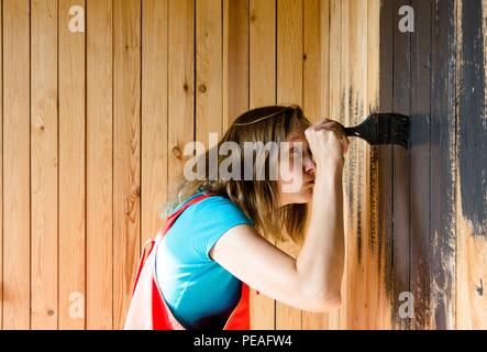 Une jeune et belle fille avec un gland dans ses mains était très concentré sur la peinture de la surface en bois en peinture noire. La fille est vêtue d'un blue ba Banque D'Images