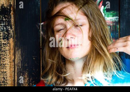 Une belle et jeune fille avec une coiffure désordonnée dont les cheveux tombent sur son visage, elle se trouve à côté de la peinture du mur peint et son visage est s Banque D'Images