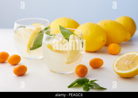 Deux verres de limonade avec les feuilles de menthe, des cubes de glace et de tranches de citron entouré de kumquats et citrons sur fond bleu Banque D'Images