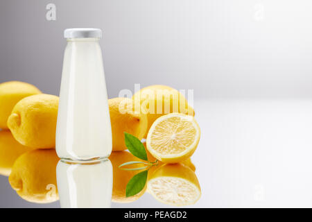 Le flacon en verre de limonade fraîche avec des citrons sur une surface réfléchissante et sur gris Banque D'Images