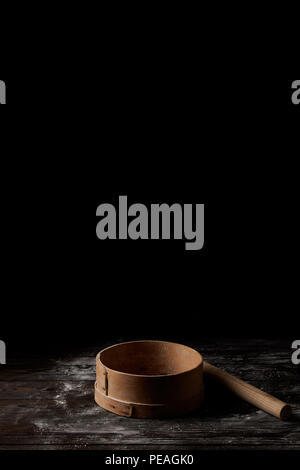 Photo de gros plan de la grille et de rouleau à pâtisserie sur la table en bois couvrant la farine par isolé sur fond noir Banque D'Images