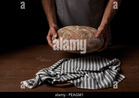 Vue partielle de l'homme de Baker holding tablier pain sur table en bois Banque D'Images