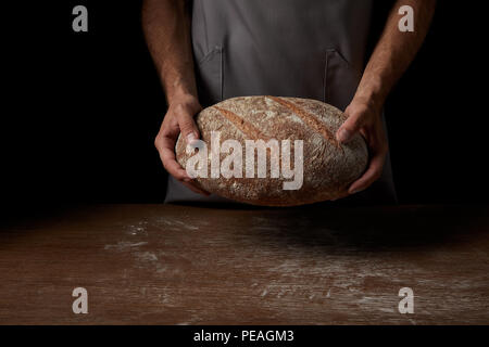 Cropped shot of male Baker à l'apron holding pain sur table en bois Banque D'Images