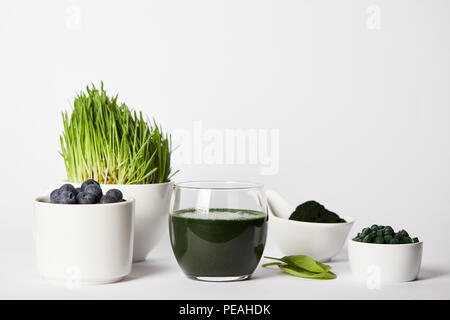 Smoothie frais à partir de la spiruline, spiruline tasses avec de l'herbe et des bleuets, des feuilles, des verres à la spiruline et la spiruline poudre comprimés sur fond gris Banque D'Images