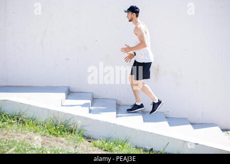 Side view full length portrait of muscular young man running up et vers le bas d'escaliers au cours de cardio plein air, copy space Banque D'Images