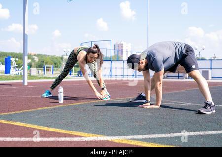 Portrait du jeune couple moderne faisant des exercices d'étirement avant le jogging extérieur dès les beaux jours de l'été, copy space Banque D'Images