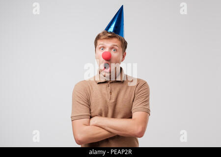 Homme mûr dans anniversaire cap et nez de clown rouge est choqué avec don. Il est donné quelque chose de très cher Banque D'Images