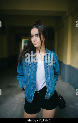 Jeune femme portant des shorts et tenir les mains dans les poches de la veste en denim bleu indifférent expression sur son visage à la voiture. Teen Girl standing in Banque D'Images