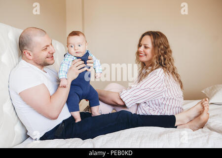 Portrait de l'âge moyen de la famille caucasienne père et mère assis sur le lit dans la chambre, maintenant prendre bébé nouveau-né fils lui faisant rire, funny touchi Banque D'Images