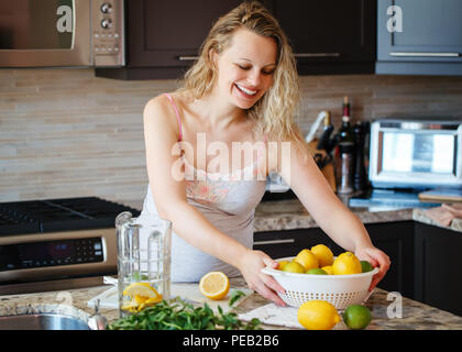 Portrait of smiling white Caucasian blonde femme enceinte avec les agrumes citron jus de lime faire debout dans la cuisine à la maison à la voiture, en bonne santé lifest Banque D'Images