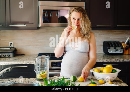 Portrait of white Caucasian blonde pregnant woman eating citron jus de citron faire in à la maison à la voiture, mode de vie sain concept Banque D'Images