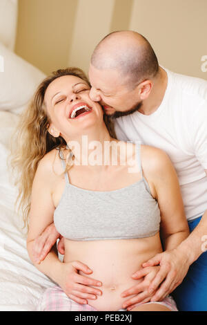 Portrait of laughing Caucasian blanche jeune couple d'âge moyen, femme enceinte avec son mari dans la chambre à couch hugging câlins, style de materni Banque D'Images