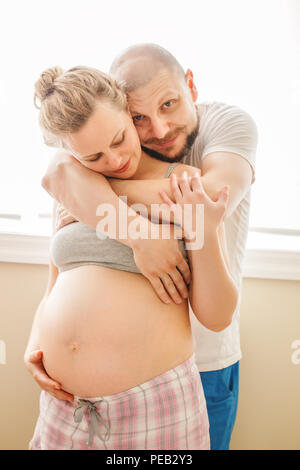 Portrait of laughing Caucasian blanche jeune couple d'âge moyen, femme enceinte avec son mari dans la chambre hugging câlins, maternité vie concep Banque D'Images