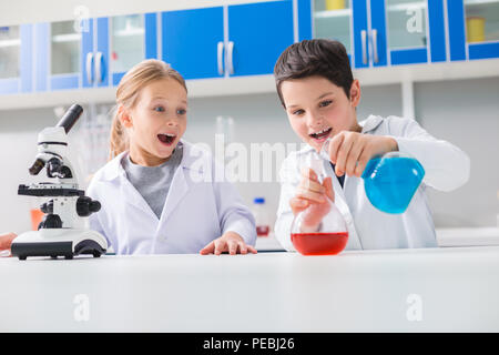 Intéressant la chimie. Joyeux positif smart boy holding flacons et le mélange des réactifs chimiques tout en étant dans le laboratoire Banque D'Images