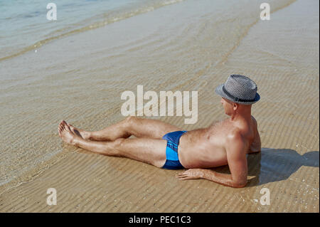 Vie d'été portrait de jeune homme bronzé dans un chapeau. Profiter de la vie et assis sur la plage, le temps de voyage. Face à la mer Banque D'Images