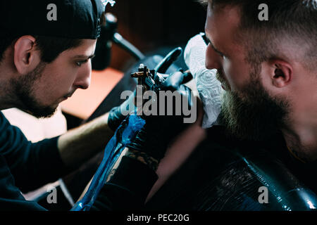 Vue latérale d'artiste de tatouage/tattoo machine avec des gants en travaillant sur tatouage sur l'épaule dans Beauté Banque D'Images