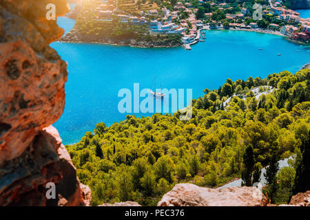 Vue d'Epic blue bay village d'Assos Kefalonia en chaud soleil matinal de la lumière. Yacht blanc à l'ancre dans le calme magnifique lagon entouré de pins et de cyprès. Grèce Banque D'Images