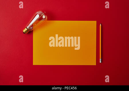 Vue de dessus du papier jaune à blanc avec crayon et lampe à incandescence sur surface rouge Banque D'Images