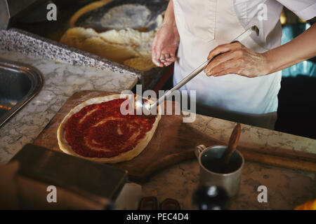 Cropped shot of chef pouring ketchup sur la pâte à pizza au restaurant de cuisine Banque D'Images