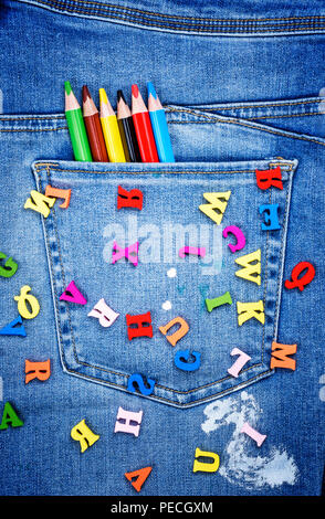 Lettres en bois multicolores de l'alphabet anglais sont dispersés sur les blue-jeans, dans une pochette de crayons, full frame Banque D'Images