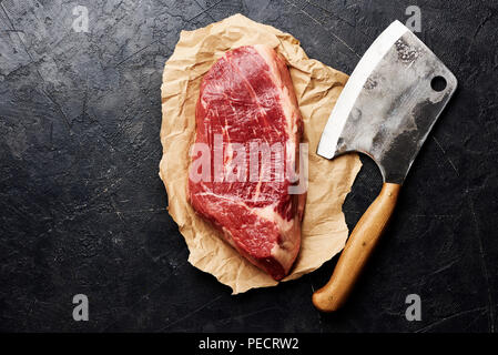 Frais crus de viande marbrée Black Angus Steak et viande cleaver sur papier brun. La viande sur fond noir avec l'exemplaire de l'espace. Vue d'en haut. Banque D'Images