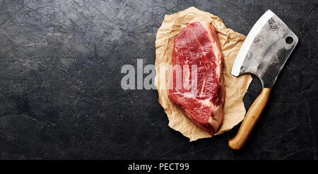 Frais crus de viande marbrée Black Angus Steak et viande cleaver sur papier brun. La viande sur fond noir avec l'exemplaire de l'espace. Vue d'en haut. Banque D'Images