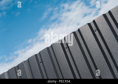 Plaque de métal brun contre blue cloudy sky. D'évitement. Surface sans couture d'acier galvanisé. Bâtiment industriel mur fait de feuille de métal ondulé, texture de fond photo Banque D'Images