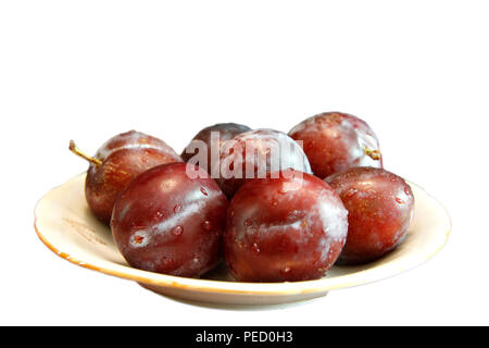 Les prunes noires frais mûrs dans une assiette blanche isolé sur fond blanc Banque D'Images