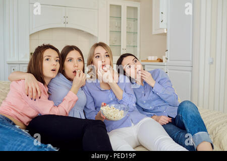 Les jeunes filles de regarder la télévision, eating popcorn assis sur le canapé. Banque D'Images