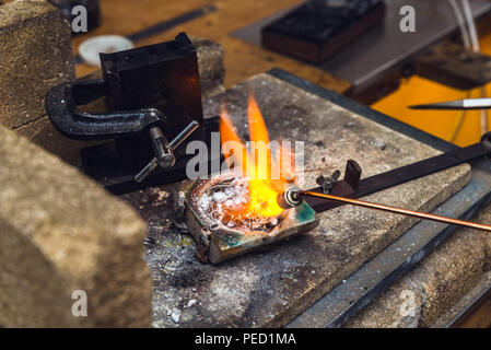 Fondre du métal en laiton avec une flamme torche dans un creuset au lieu de travail d'orfèvre pour l'exécution de la ferronnerie artisanale Banque D'Images