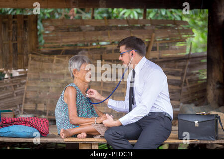 Femme plus âgée reçoit la visite du médecin au patient accueil ou à l'extérieur. Un médecin ou un professionnel de la santé des bénévoles pour visiter les personnes âgées dans les zones rurales d'Asie. Banque D'Images