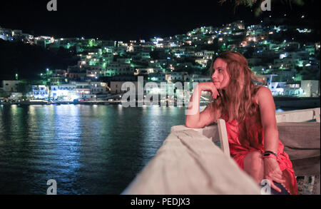 Une jeune fille portant une robe rouge fixe avec sa main tenant sa tête vers la mer Égée, dans l'île d'Astipalea, Grèce, en été la nuit t Banque D'Images