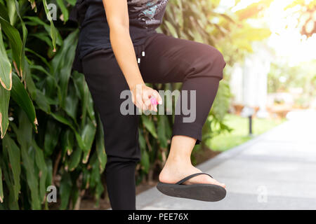 Femme de pulvériser un insecticide contre les piqûres de moustiques sur sa jambe dans le jardin Banque D'Images