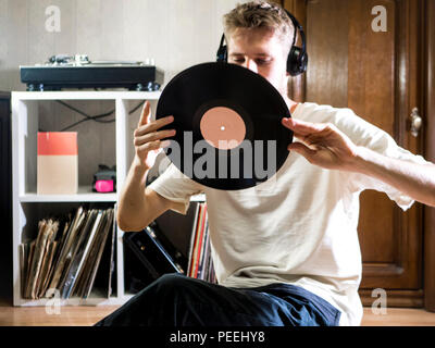 Jeune homme assis dans la salle de séjour confortable en maintenant le disque vinyle dur près du rack documents sur le plancher Banque D'Images