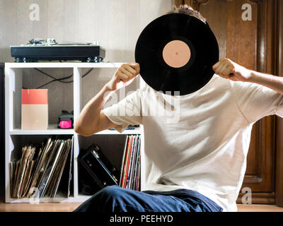 Jeune homme assis dans la salle de séjour confortable en maintenant le disque vinyle dur près du rack documents sur le plancher Banque D'Images