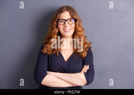 Portrait of happy young woman with folded arms posing at mur gris. Banque D'Images