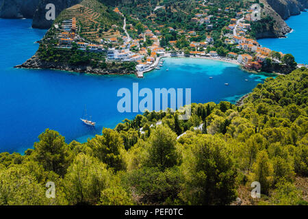 Vue de dessus à couper le souffle d'Assos village avec des maisons locales. Lieu historique de Kefalonia. Lonely yacht blanc à l'ancre dans un lagon magnifique entouré de pins et de cyprès. Grèce Banque D'Images