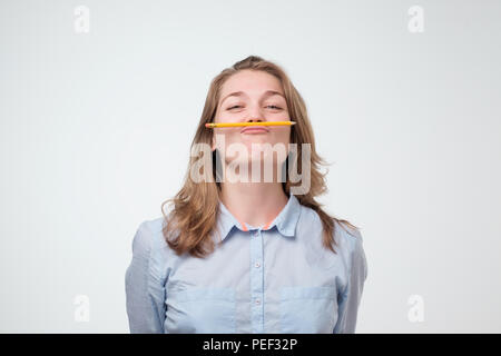 Jeune belle étudiante tenir pen entre le nez et les lèvres comme à la moustache drôle et coquine après des études longues heures isolé sur fond blanc Banque D'Images