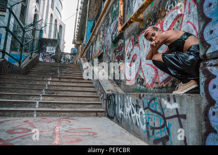 Street Punk fille assise près de l'escalier en béton. Mode de vie urbain en ville avec graffiti peint passage sous le pont Banque D'Images