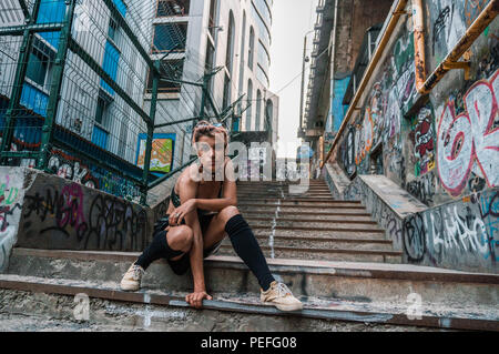 Plan large de street punk girl en milieu urbain. Fille assise sur l'escalier peint avec de l'écriture graffiti sous le pont Banque D'Images