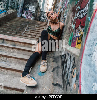 Plan large de street punk girl en milieu urbain. Fille assise sur l'escalier peint avec de l'écriture graffiti sous le pont Banque D'Images