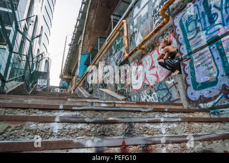 Plan large de street punk girl en milieu urbain. Fille assise sur l'escalier peint avec de l'écriture graffiti sous le pont Banque D'Images