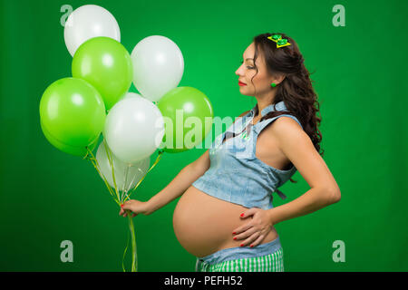 Femme enceinte avec des ballons sur un fond vert. Il regarde son ventre, en prévision. Banque D'Images