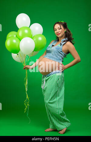 Femme enceinte avec des ballons sur un fond vert. Il regarde son ventre, en prévision. Banque D'Images