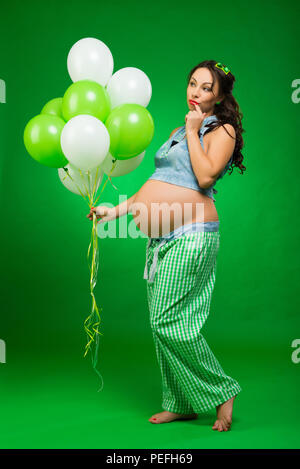 Femme enceinte avec des ballons sur un fond vert. Il regarde son ventre, en prévision. Banque D'Images