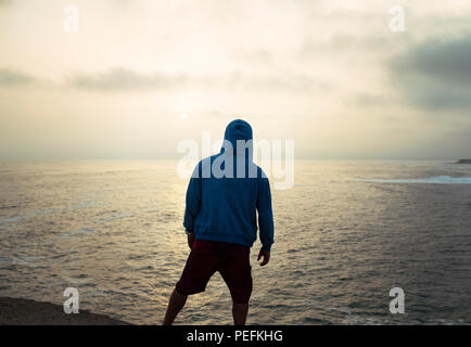 Silhouette d'un homme fit in hoodie nonchalamment debout, regardant le coucher du soleil sur l'océan. Punta Hermosa Beach, ville de la province de Lima, Pérou. Jul 2018 Banque D'Images