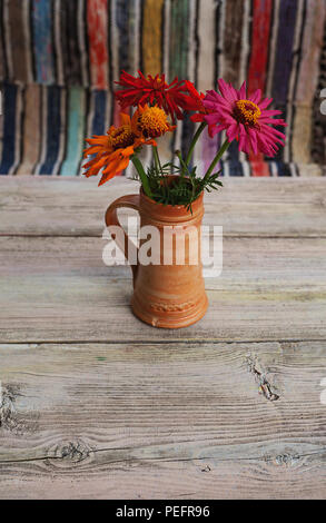 Des fleurs colorées dans la vieille tasse en céramique sur la vieille table en bois, tapis colorés en arrière-plan. Banque D'Images