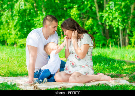 Famille heureuse sur la couverture se reposant dans le parc, mère enceinte Banque D'Images