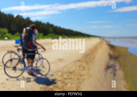 Voyage couple en vélo sur la plage par la mer sur un fond de ciel bleu et les dunes vont en voyage. Flou Banque D'Images